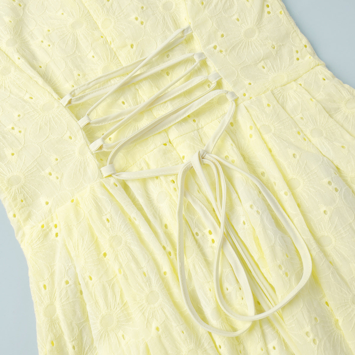 Close-up of a light yellow dress with lace details on a light blue background