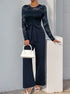 A navy blue version of the lace jumpsuit, styled similarly with white accessories, posing elegantly.