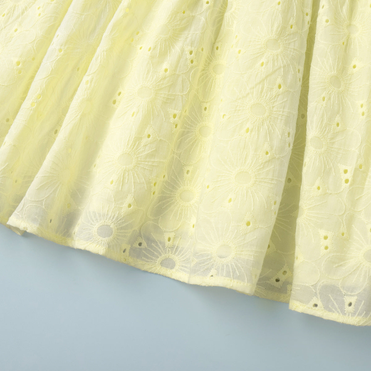 Close-up of a yellow lace fabric with floral patterns on a light blue background