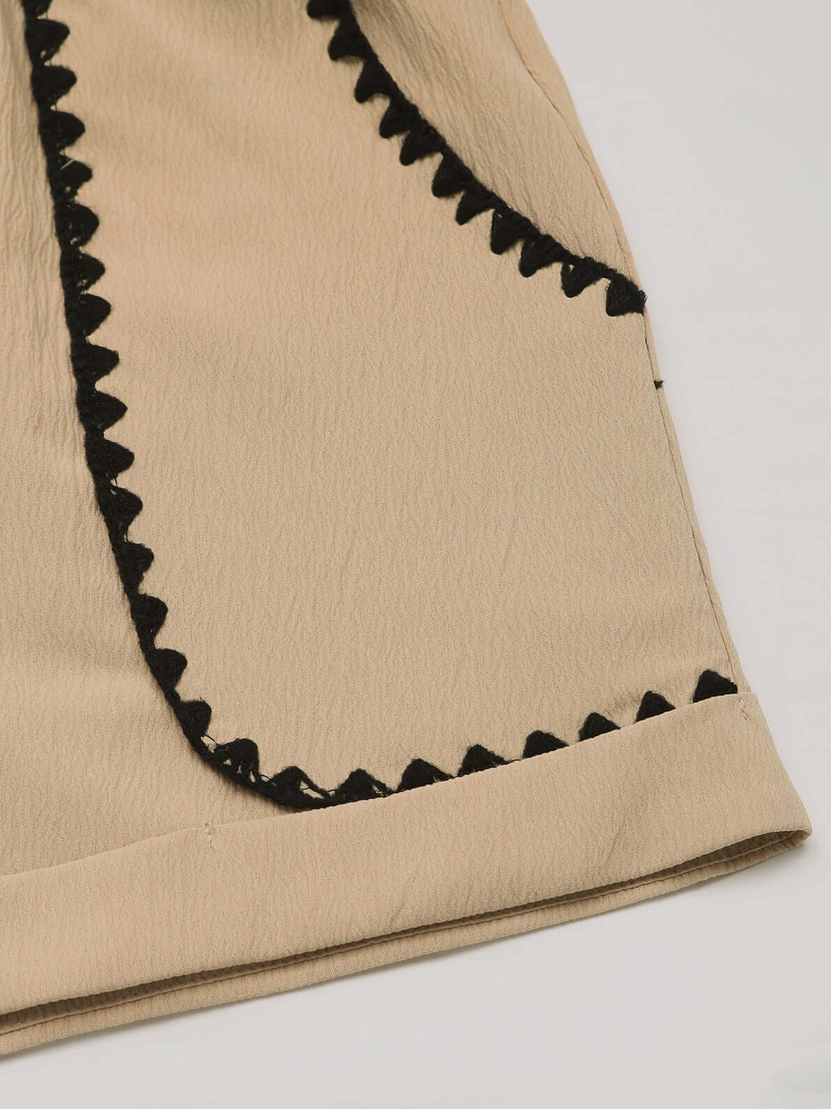 Close-up of the hem of beige high-waisted shorts with black lace detailing and rolled edges.