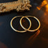 Gold hoop earrings displayed on dark surface beside ornate gold frame detail, catching warm ambient light