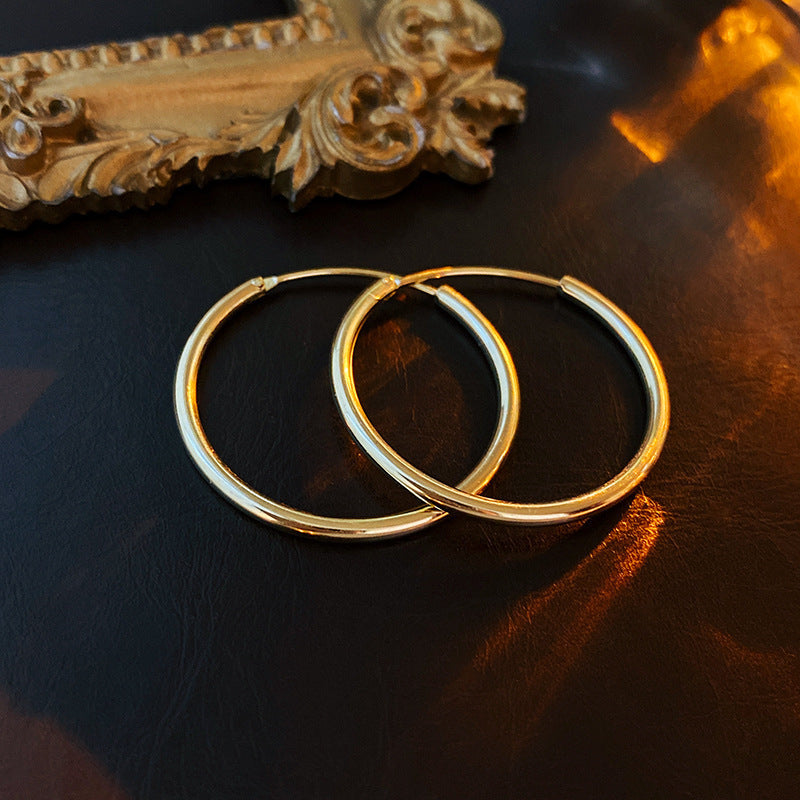 Gold hoop earrings displayed on dark surface beside ornate gold frame detail, catching warm ambient light