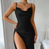 Woman in a black satin slip dress with a thigh-high slit, posing in a bedroom