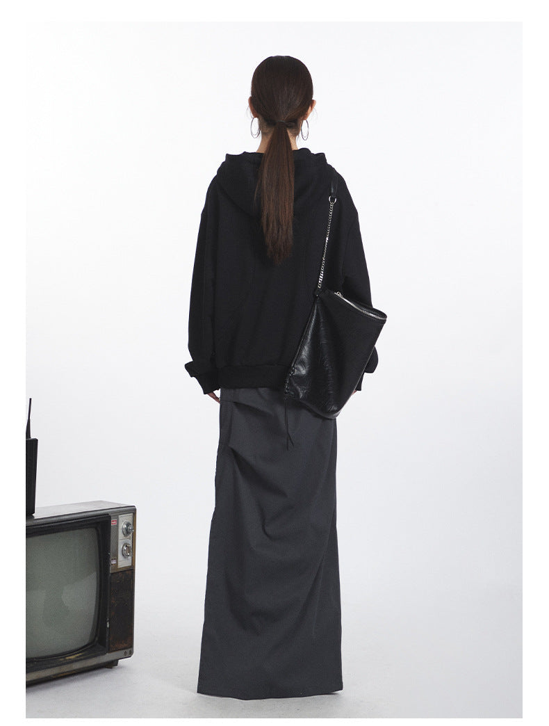 Black oversized hoodie with curved pocket design and metal snaps, paired with gray maxi skirt, shown from back view