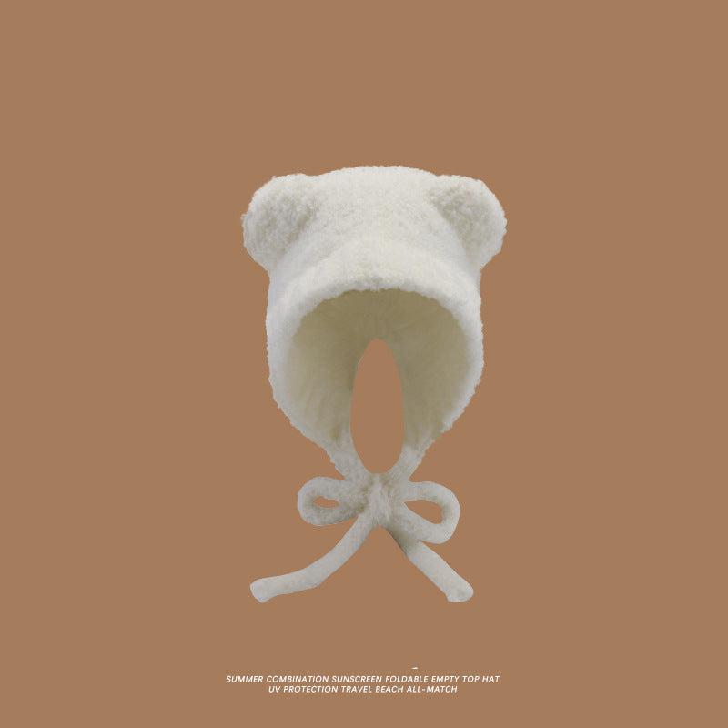A white teddy bear ear hat with matching white tie closure against brown background, highlighting soft plush material and rounded ears