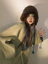 Brown plush winter hat with blue accent and braided ties, paired with light green outerwear