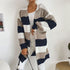 A woman in navy, gray and white striped open cardigan styled with white tank top and white jeans against neutral home background