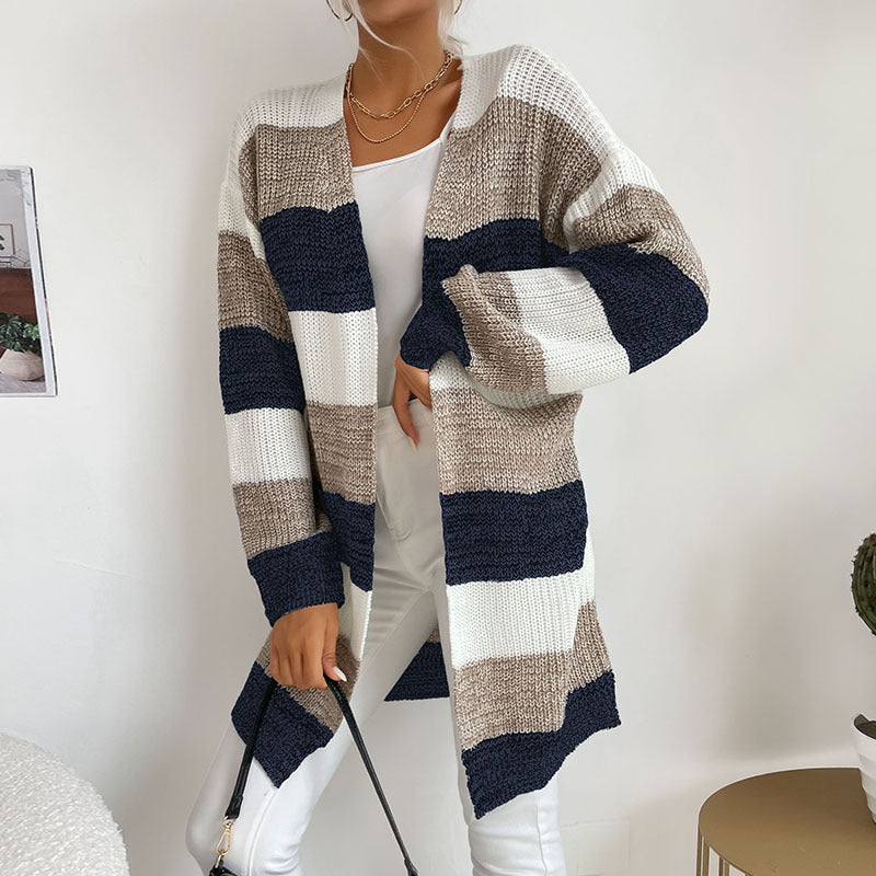 A woman in navy, gray and white striped open cardigan styled with white tank top and white jeans against neutral home background