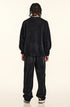 Back view of model with twisted braids wearing black sweatshirt and pants, silver chain necklace visible at collar, relaxed streetwear silhouette