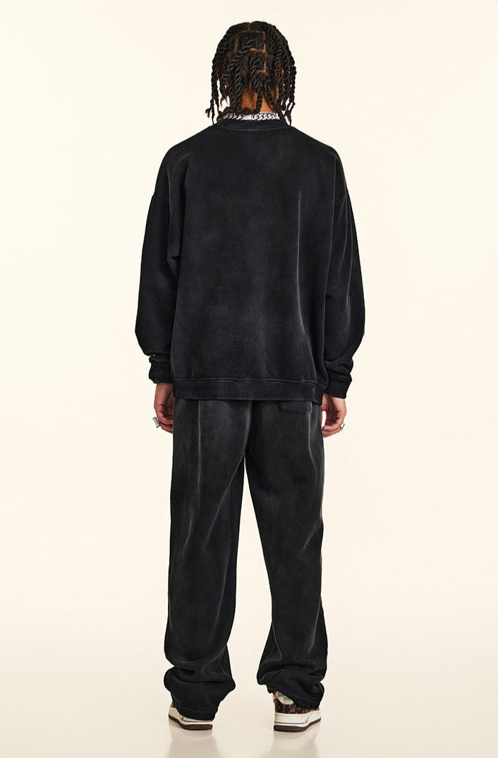 Back view of model with twisted braids wearing black sweatshirt and pants, silver chain necklace visible at collar, relaxed streetwear silhouette