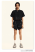 Model wearing black cropped tee and matching shorts with white socks and chunky gray sneakers against neutral background