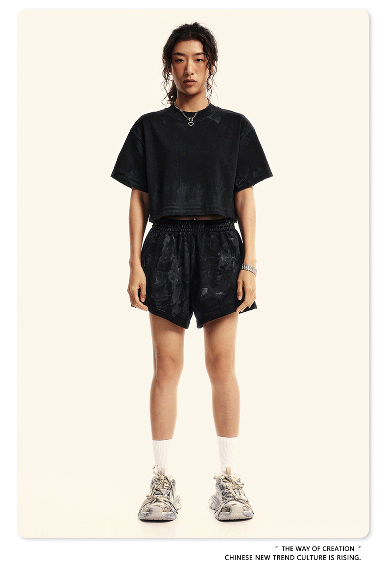 Model wearing black cropped tee and matching shorts with white socks and chunky gray sneakers against neutral background