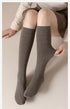 Person sitting with taupe skirt and gray knee-high socks against beige backdrop