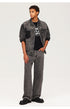 Young model wearing washed black denim jacket over graphic tee with matching wide-leg jeans and chunky boots