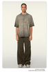 Model with braided hair wearing gray ombre t-shirt with silver chain necklace, olive cargo pants and light colored sneakers against white background