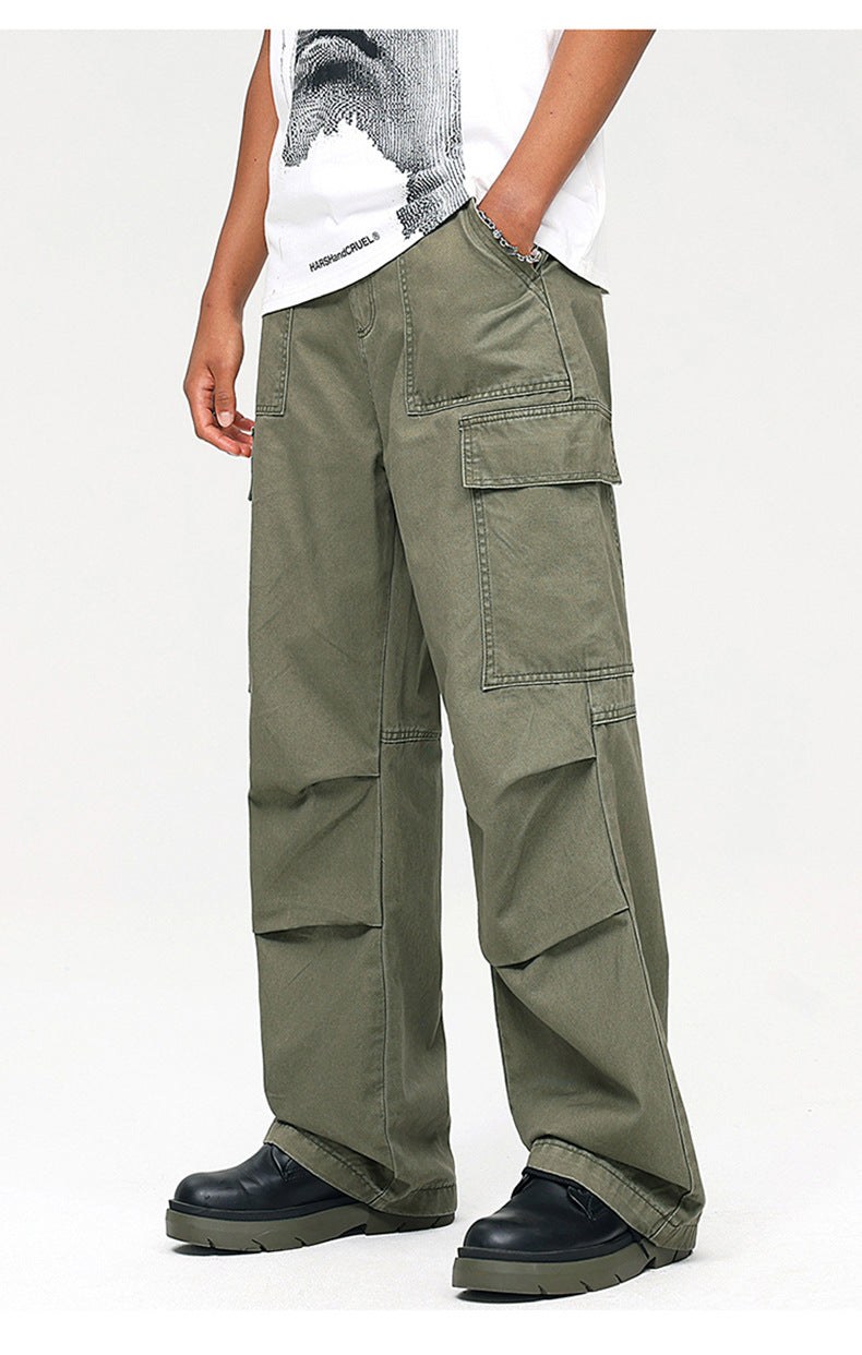A person standing in olive green multi-pocket cargo pants with white HARSHandCRUEL tee and silver bracelet against white background