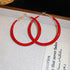 A pair of large red enamel gold hoop earrings is displayed on a textured white surface with "Thank You" printed on it