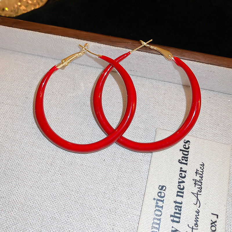 A pair of large red enamel gold hoop earrings is displayed on a textured white surface with "Thank You" printed on it