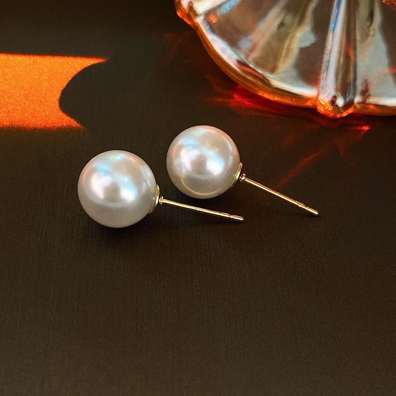 Classic white pearl stud earrings on dark surface, showing reflective finish under ambient lighting