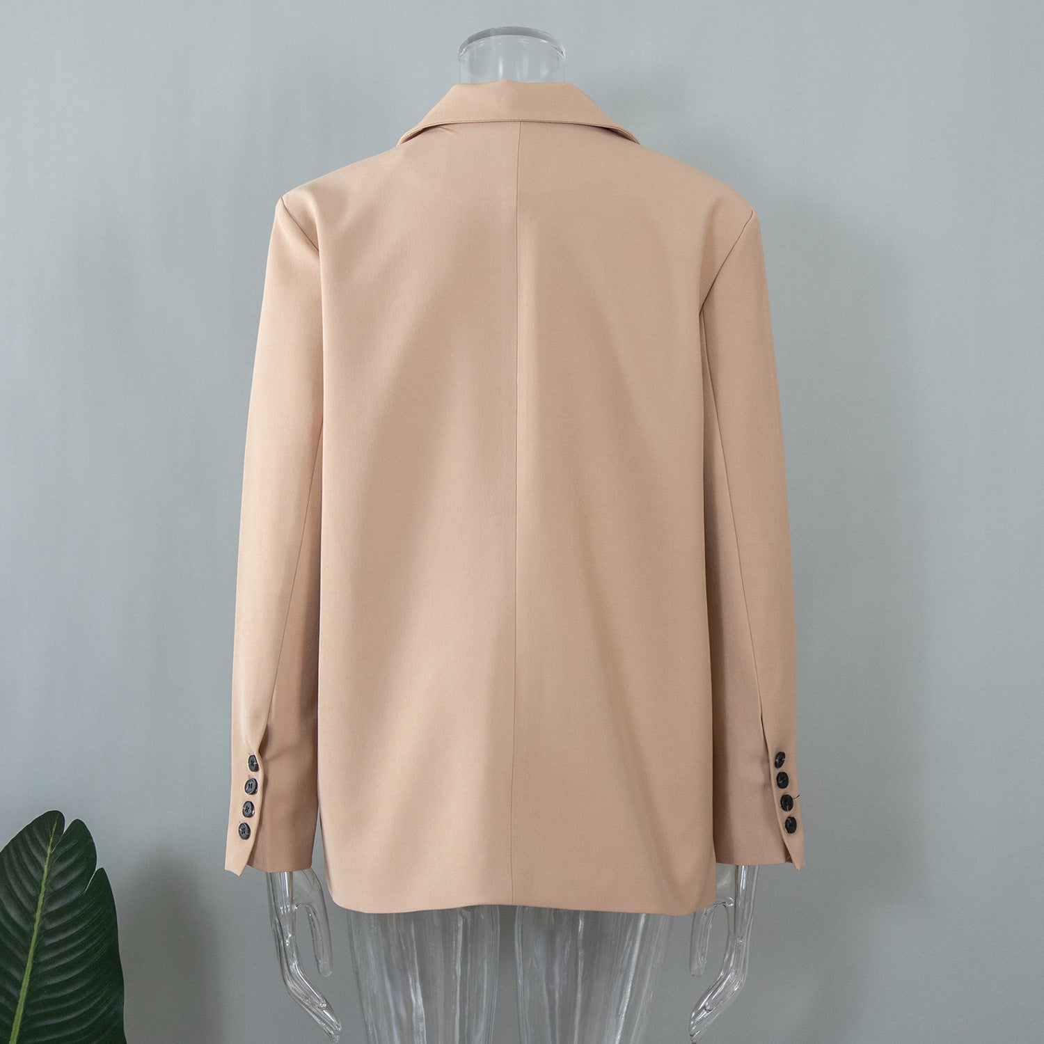 Back view of a beige oversized blazer on a transparent mannequin, highlighting clean lines and precise tailoring
