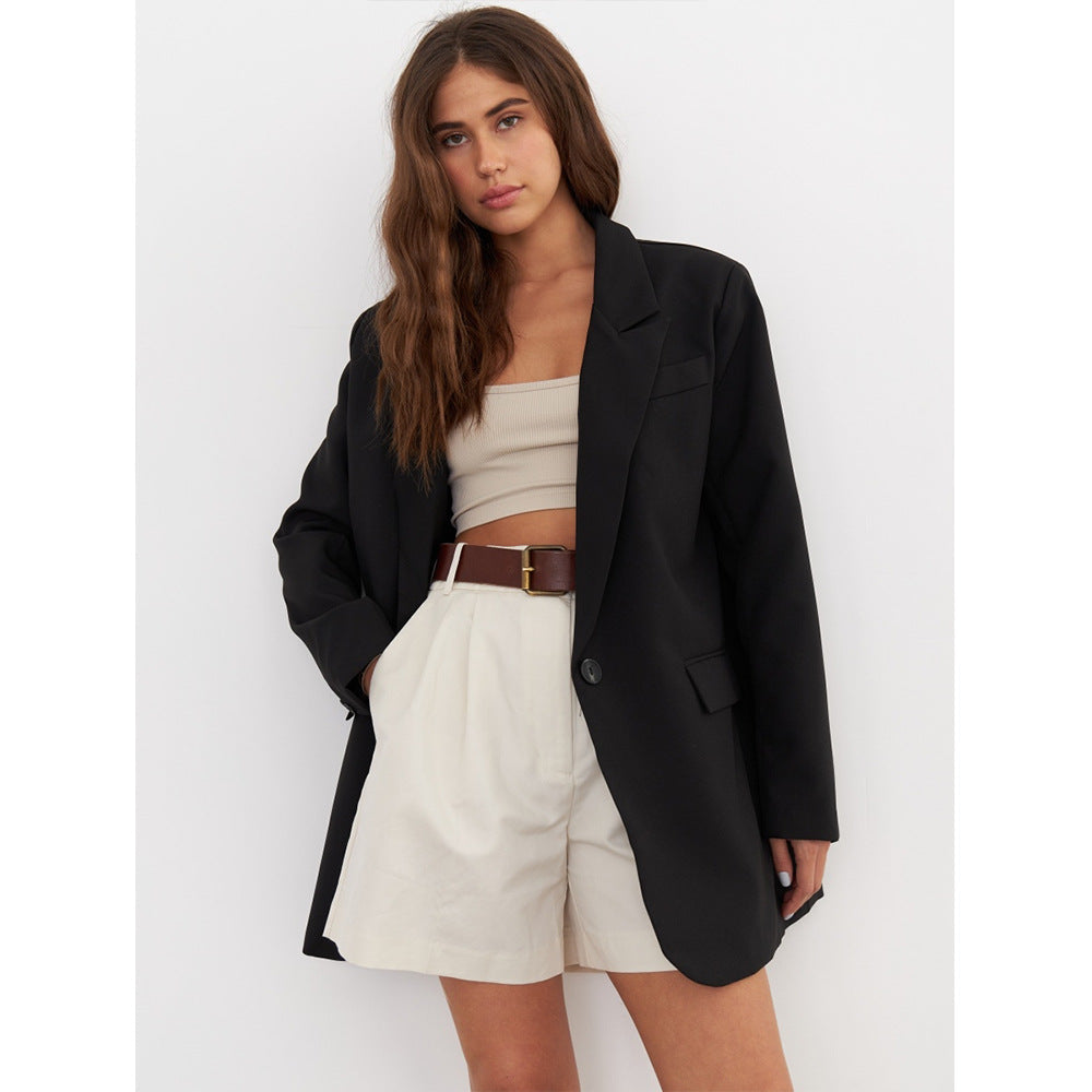 Black oversized blazer layered over a cream bandeau top and white high-waisted shorts with a brown leather belt, embodying modern minimalist style