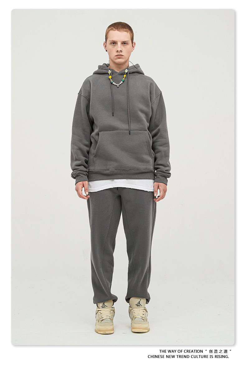 Male model with short hair wearing a charcoal gray sweatsuit with hoodie, white undershirt, and matching joggers