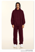 Model in burgundy hoodie and sweatpants set with white sneakers on neutral background