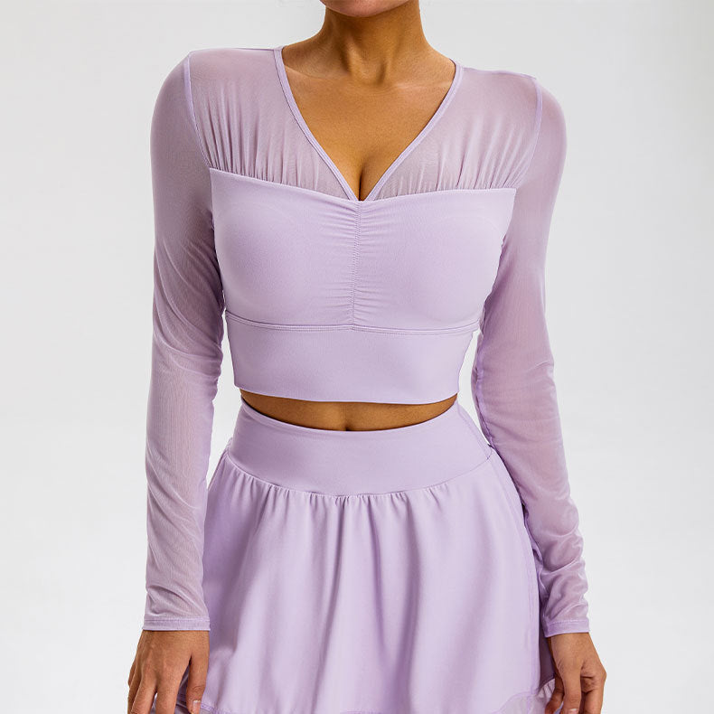 A model is wearing a lavender mesh-sleeve crop top with V-neckline and gathered bust detail, paired with matching high-waisted skirt against gray background