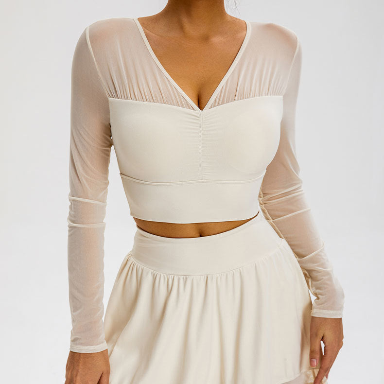 A model is wearing a cream mesh-sleeve crop top with V-neckline and ruched center detail, paired with matching high-waisted mini skirt against gray backdrop