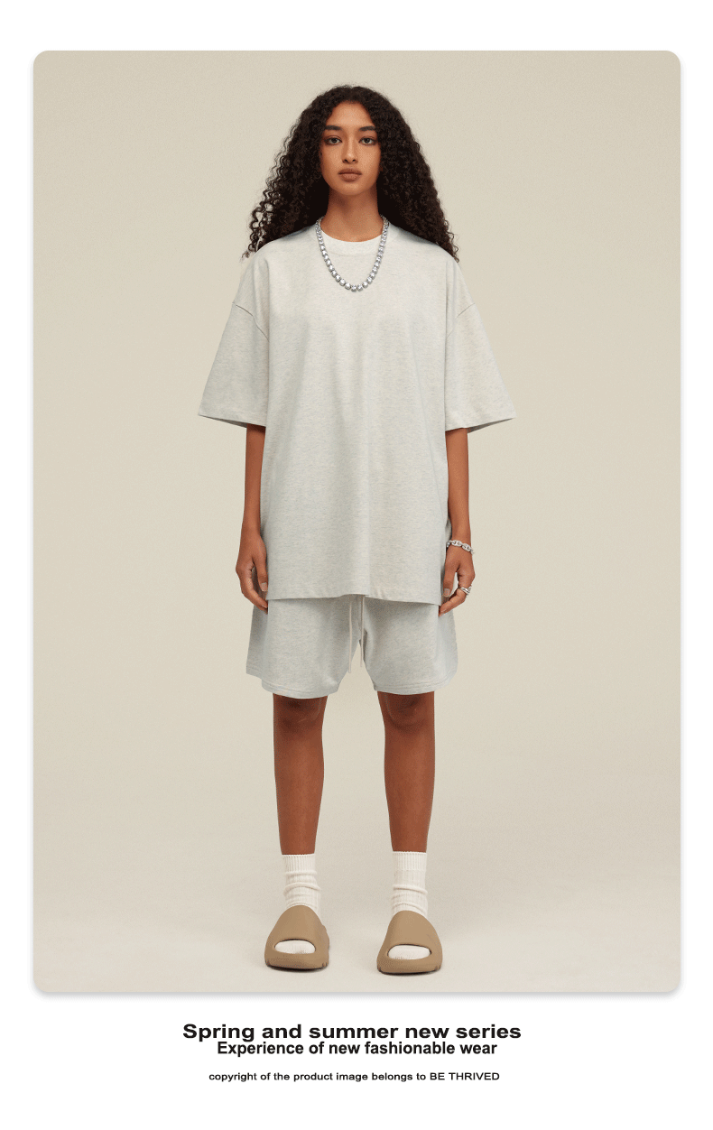 Model with curly hair wearing white oversized t-shirt and matching shorts with beige slides and white socks against cream background