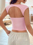 A woman showing back view of pink crop top with open cutout design, paired with white drawstring pants in bright indoor setting