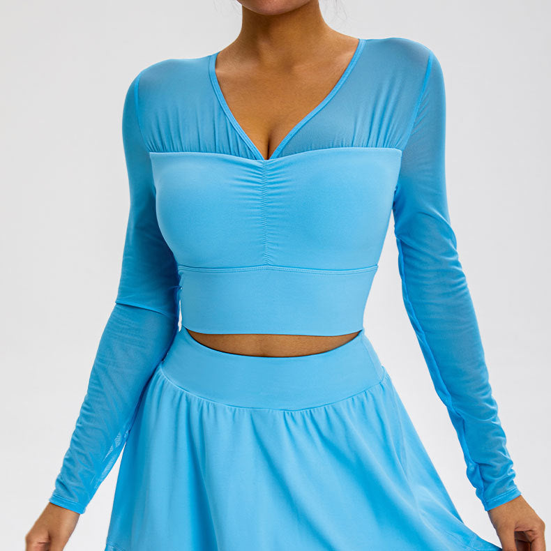 A model is wearing a sky blue mesh-sleeve crop top with V-neckline and gathered center detail, paired with matching high-waisted skirt against gray background