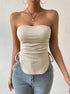 A model wearing cream ribbed tube top with side tie detail paired with light wash jeans against white wall, gold pendant necklace