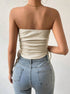Back view of model in cream ribbed strapless top with side ties and light wash high-waisted jeans, gold chain necklace
