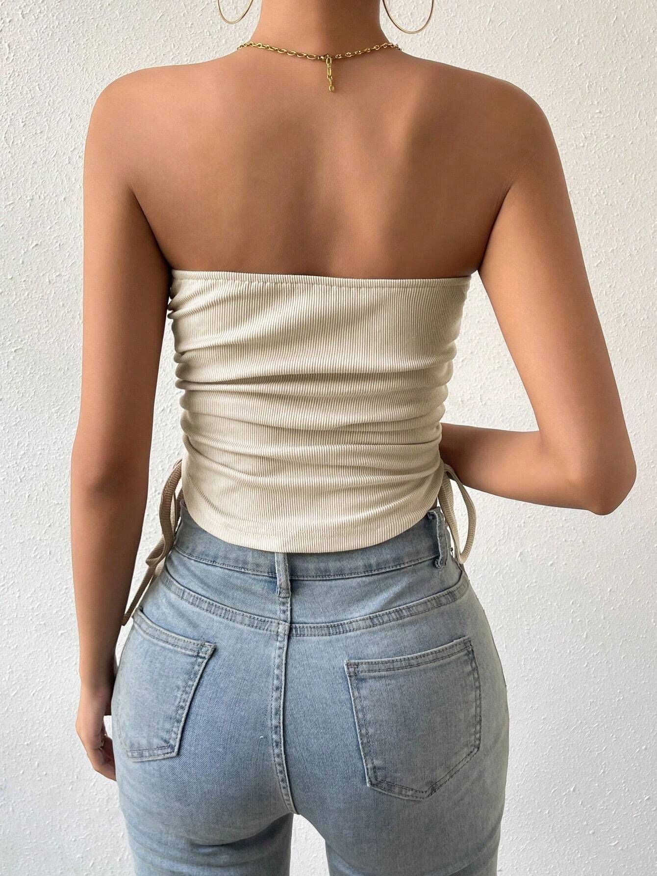 Back view of model in cream ribbed strapless top with side ties and light wash high-waisted jeans, gold chain necklace