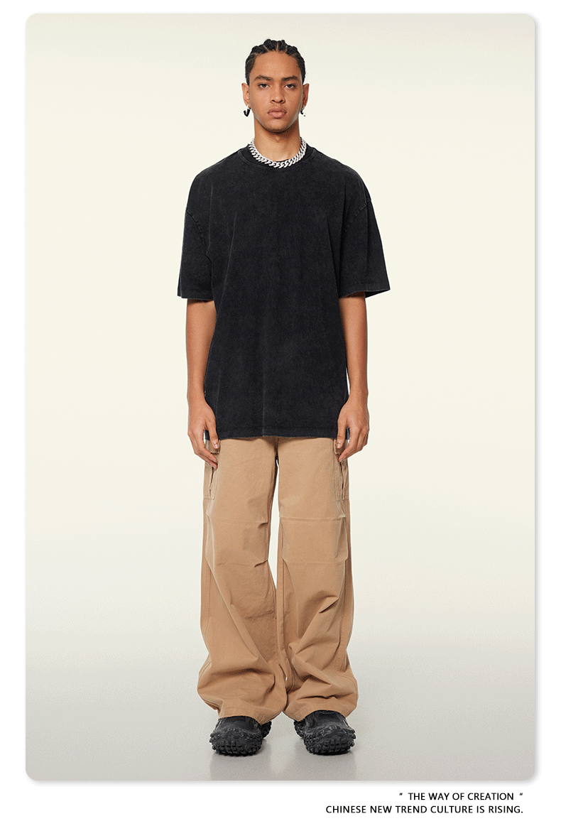 Model with braided hair wearing black oversized t-shirt, black wide-leg pants and silver chain necklace against neutral background