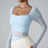 A model is wearing a light blue mesh-sleeve top with square neckline and thin straps, posing against a gray background