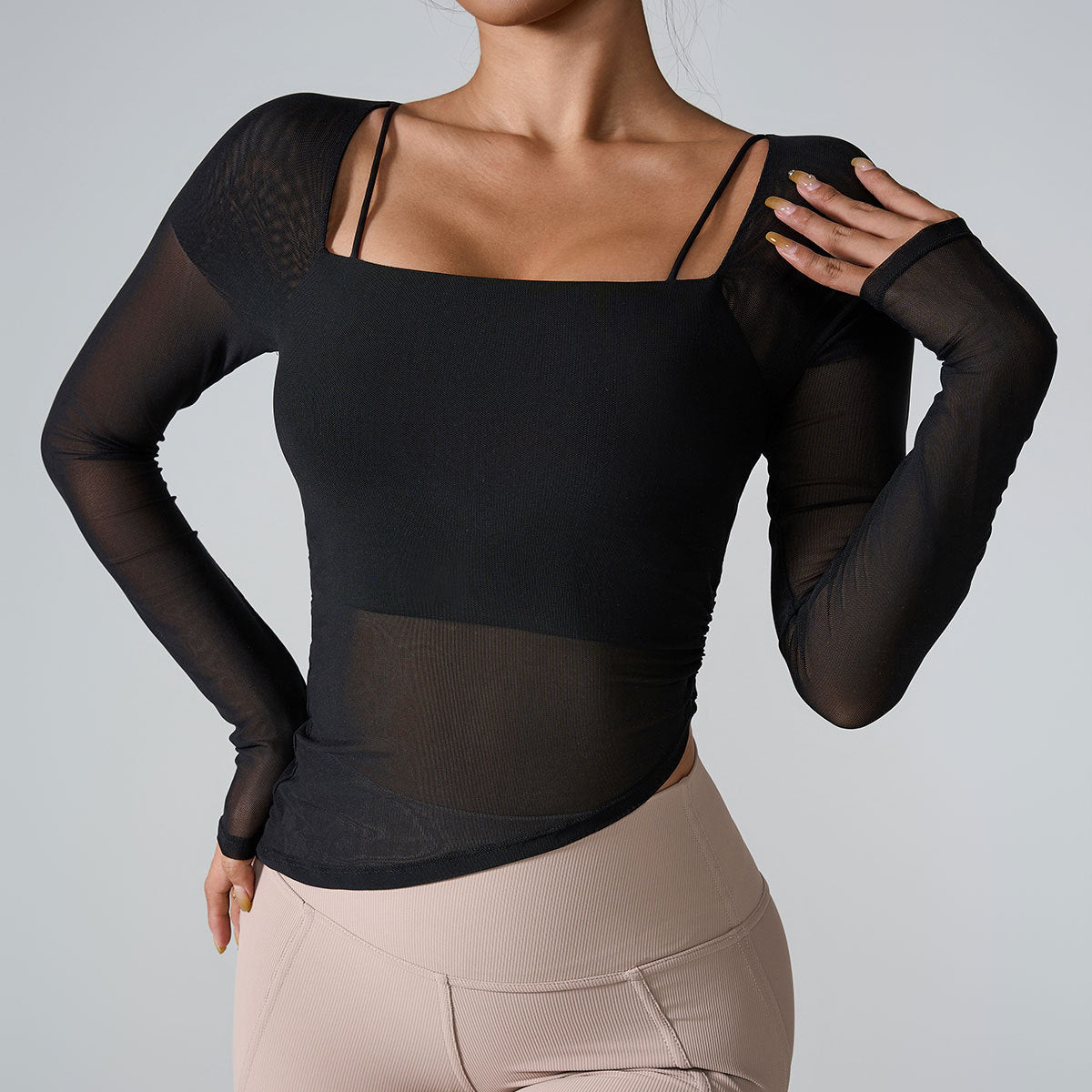 A model is wearing a black mesh-sleeve athletic top with square neckline and thin straps, posing against a gray backdrop