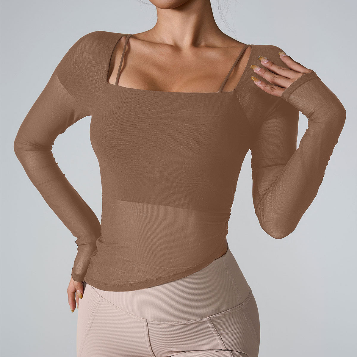 A model is wearing a brown mesh-sleeve athletic top with square neckline, paired with beige high-waisted leggings against a gray background