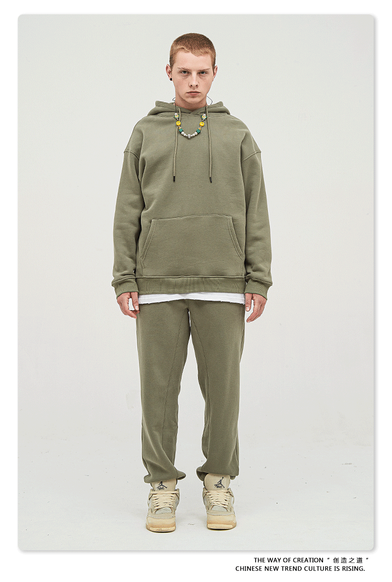 Male model with short hair wearing a sage green sweatsuit with hoodie, white undershirt, and matching joggers