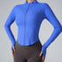 A woman wearing a cobalt blue ribbed zip-up athletic top with contoured seams and thumb holes paired with dark brown leggings against a gray backdrop