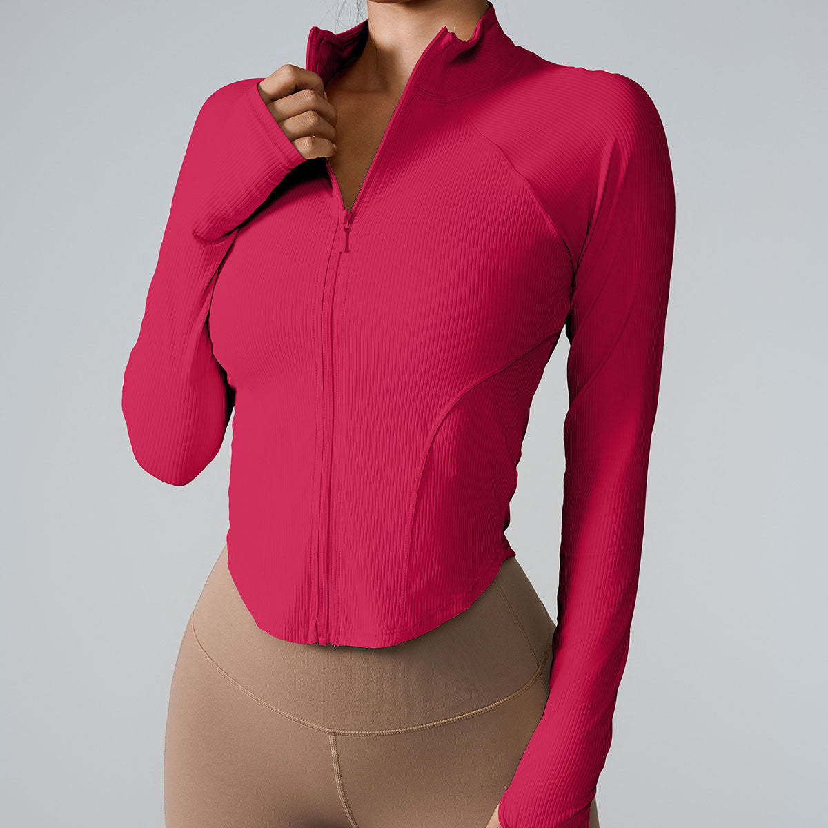 A woman wearing a raspberry pink ribbed zip-up athletic jacket with contoured panels paired with beige high-waisted leggings against a gray background