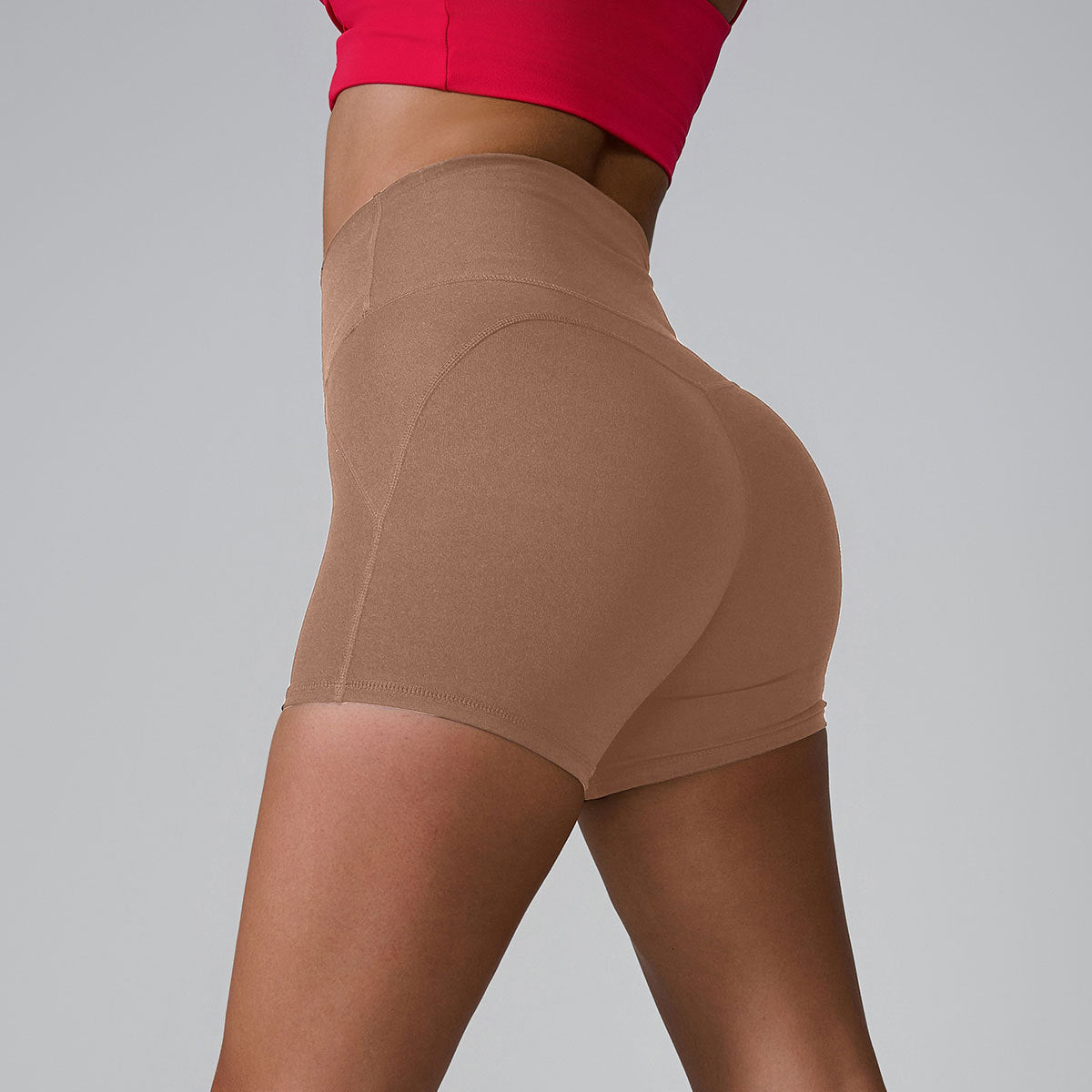 Nude-colored high-waisted compression shorts in profile view, paired with red sports bra against gray backdrop