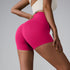 Model wearing hot pink compression shorts with high waistband and cream sports bra, showing side view against gray backdrop