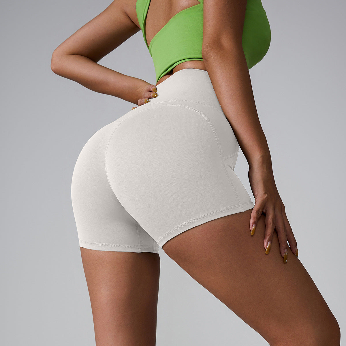 Cream-colored high-waisted athletic shorts with seamless design, paired with lime green sports top, side profile view
