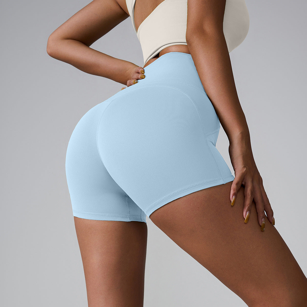 Baby blue compression shorts with high waist shown from side angle, model wearing cream sports bra against gray background