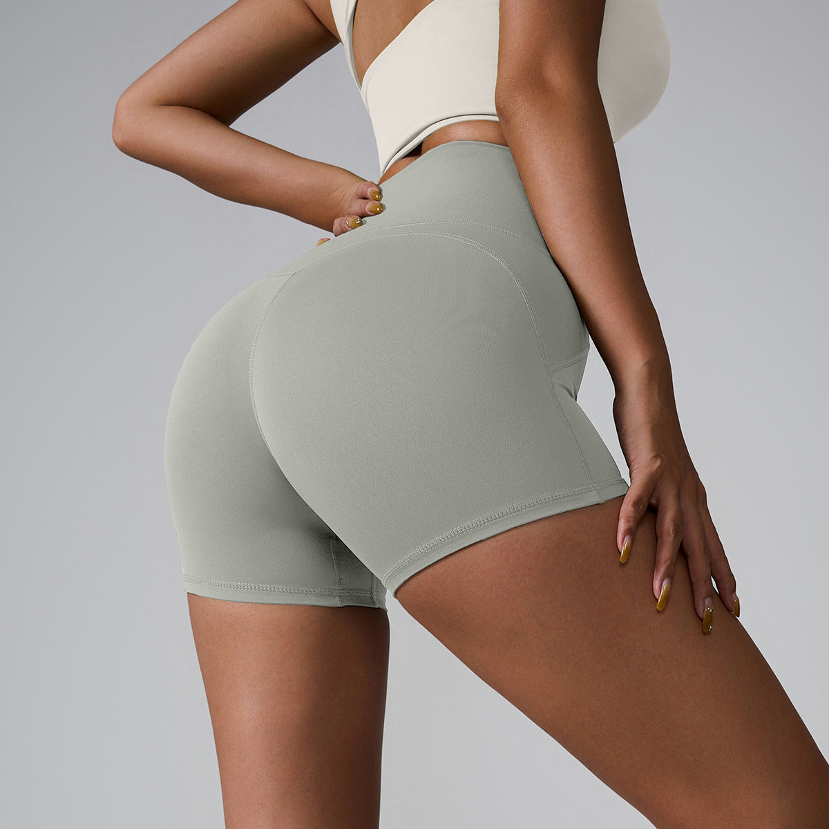 Light gray athletic shorts with contoured seams, shown in side profile with cream sports top and gold nail detail