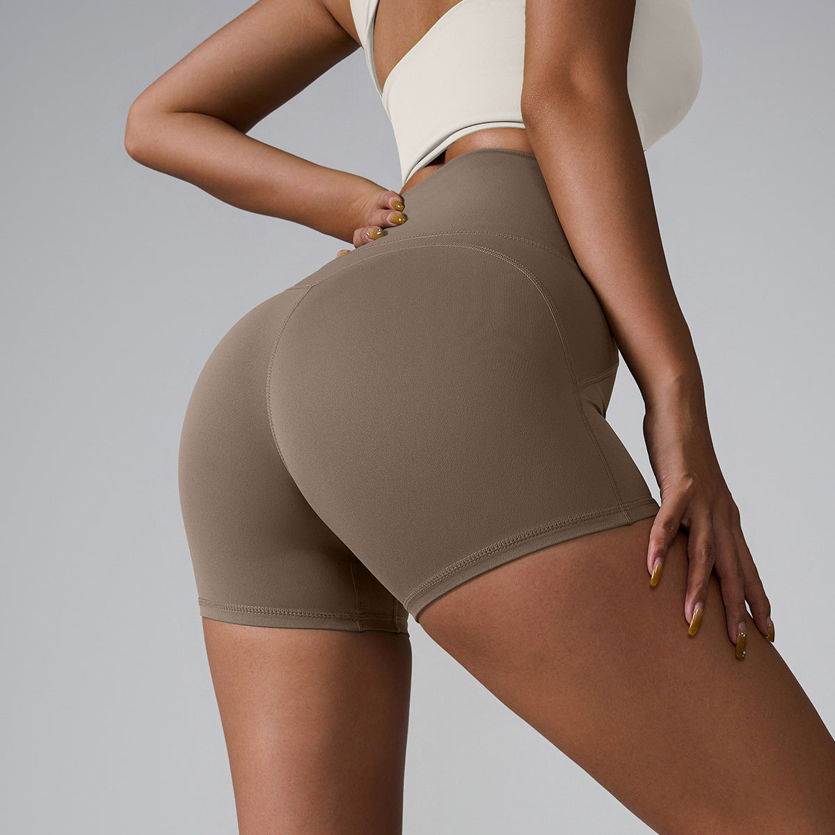 Taupe high-waisted compression shorts with contoured seams, paired with cream sports bra, side view