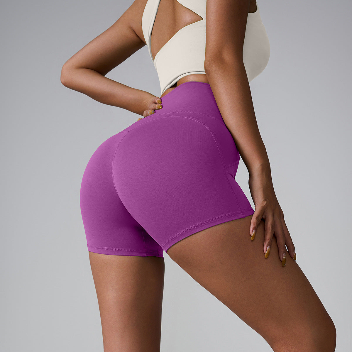 Purple high-waisted compression shorts with contoured design, paired with cream sports top, side profile view