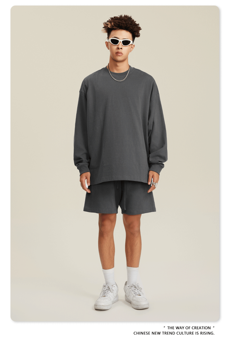 Man in dark gray sweatshirt and shorts set with sunglasses, chain necklace and white sneakers